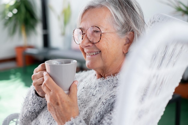 femme séduisante senior avec un sourire joyeux se relaxant dans le fauteuil du balcon tenant un café