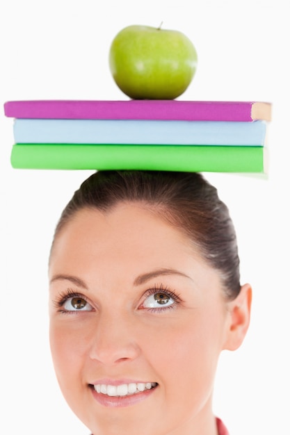 Femme séduisante tenant une pomme et des livres sur sa tête en position debout