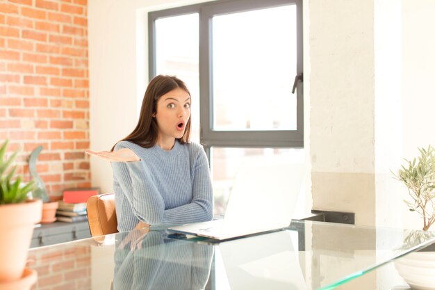 femme semblant surprise et choquée, avec la mâchoire tombée tenant un objet avec une main ouverte sur le côté