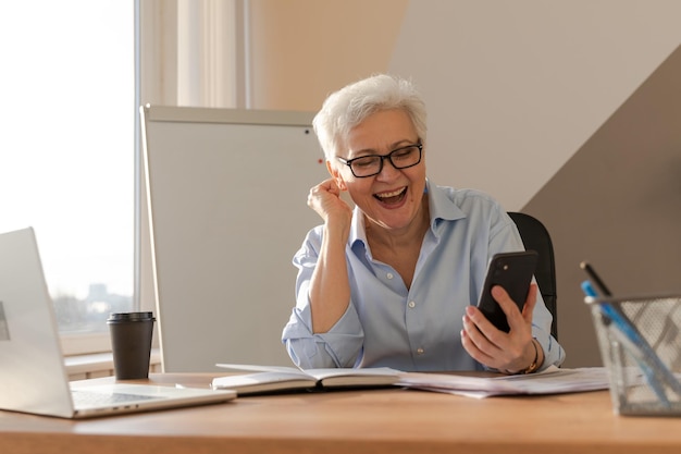 Femme senior d'âge moyen confiante gagnante euphorique avec une dame mature plus âgée regardant la cellule