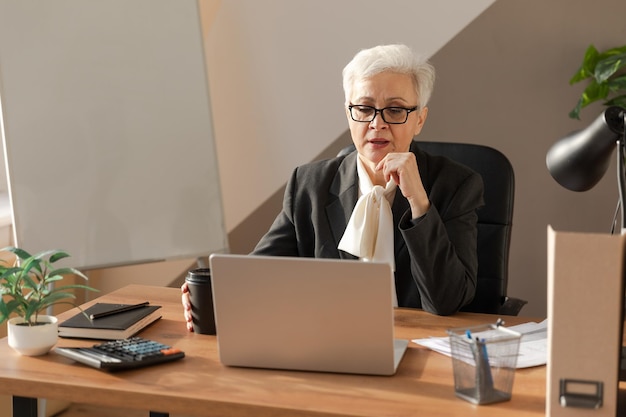 Femme senior d'âge moyen européen élégant et confiant utilisant un ordinateur portable sur le lieu de travail élégant s mature plus âgé