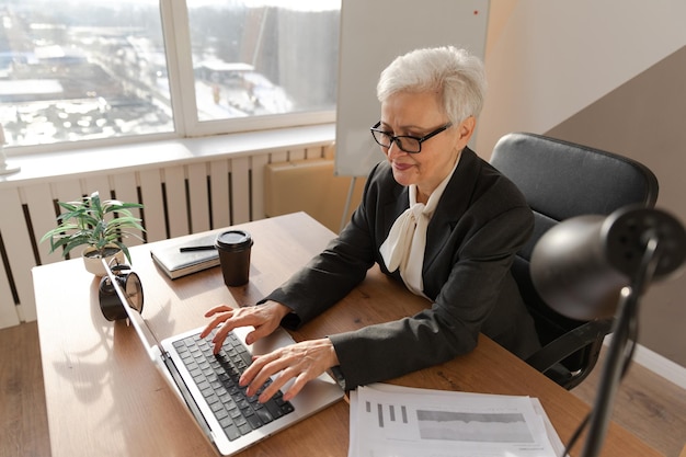 Femme senior d'âge moyen européen élégant et confiant utilisant un ordinateur portable sur le lieu de travail élégant s mature plus âgé