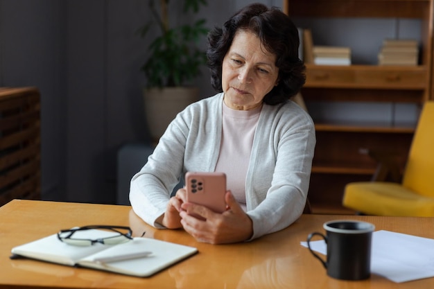 Femme senior d'âge moyen européenne tenant à l'aide d'un écran tactile de smartphone tapant la page de défilement o élégant