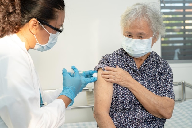 Une femme senior asiatique âgée portant un masque facial se faisant vacciner contre le covid19 ou le coronavirus par un médecin fait une injection