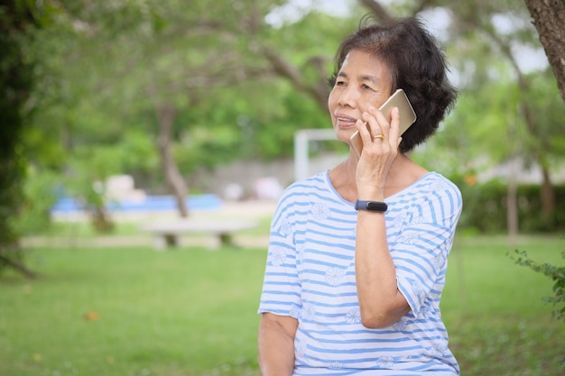 Femme senior asiatique souriante à l'aide de smartphone assis au jardin