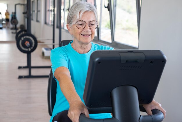 Femme senior athlétique souriante dans une salle de sport faisant du vélo d'exercice en profitant du sport et d'un mode de vie sain