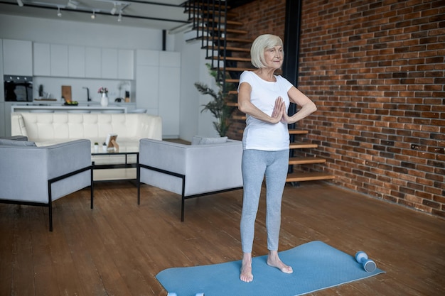 Femme senior aux cheveux gris debout avec ses mains en namaste