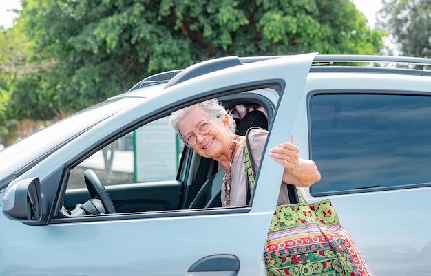 Une femme senior caucasienne souriante entrant dans sa voiture une grand-mère heureuse avec un grand sac fait main ouvre la porte pour entrer dans le véhicule prêt à conduire