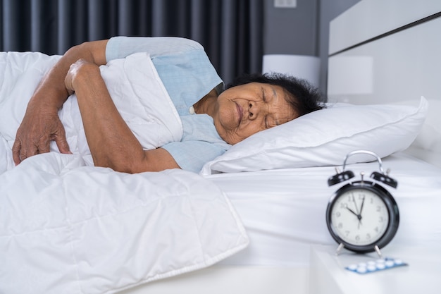 femme senior, dormir sur un lit avec une horloge