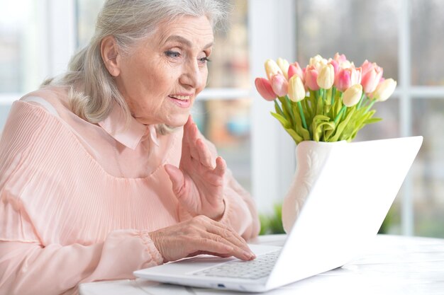 Femme senior émotionnelle assise à table avec ordinateur portable