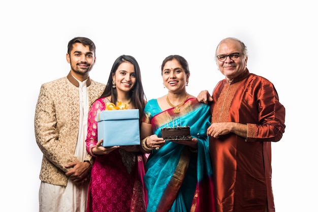 Femme senior indienne avec sa famille célébrant son anniversaire en soufflant des bougies sur un gâteau tout en portant des vêtements ethniques