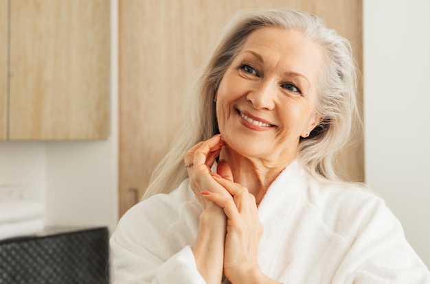 Femme senior joyeuse aux cheveux gris regardant un miroir avec les mains jointesx9xA