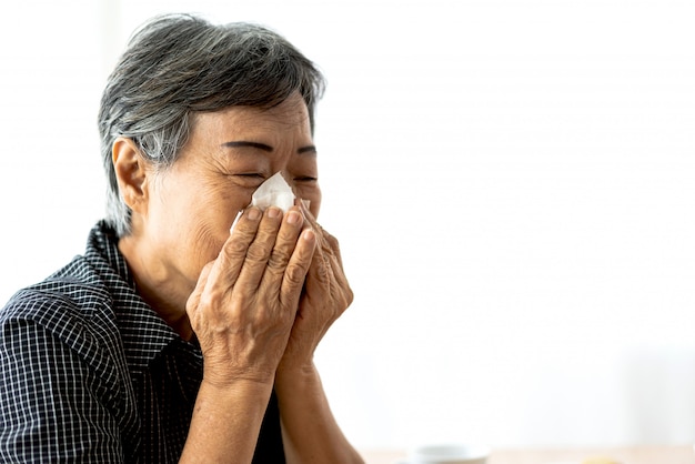 Femme senior malade se mouchant avec du papier absorbant et éternuements tout en ayant des soins de santé et des médicaments contre le rhume.