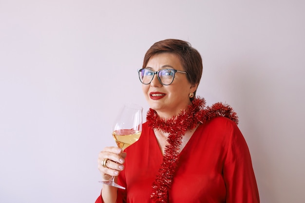 femme senior mature élégante en chemisier rouge avec verre de vin blanc célébrant le nouvel an