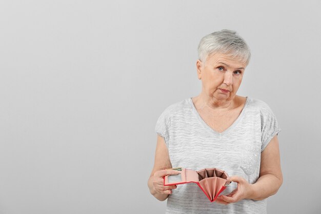 Femme senior avec portefeuille vide sur fond clair