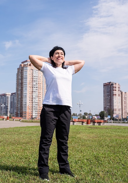 Femme senior souriante, échauffement avant de s'entraîner à l'extérieur dans le parc sur scène urbaine