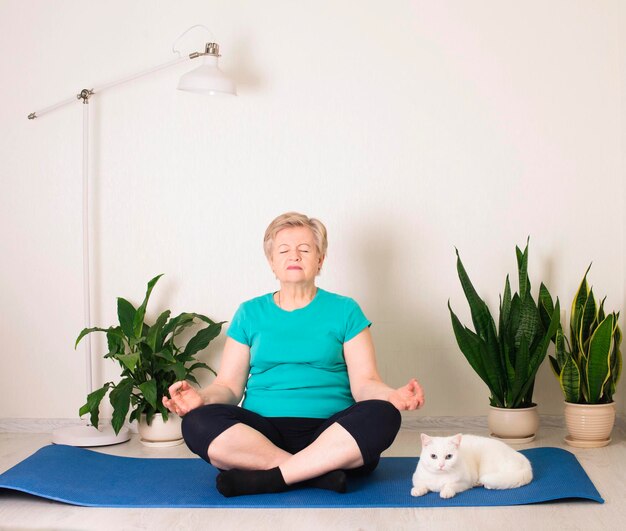 Femme senior souriante méditant se détendre avec chat Granny dans la pose de yoga faisant des exercices de respiration