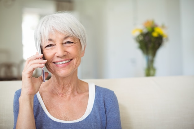 Femme senior souriante parlant au téléphone mobile dans le salon
