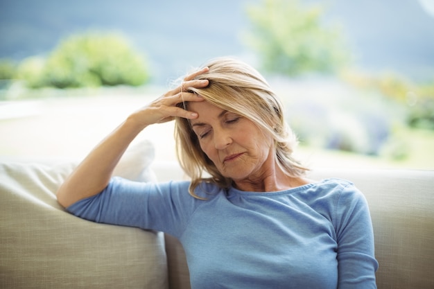 Femme senior tendue assis sur un canapé dans le salon