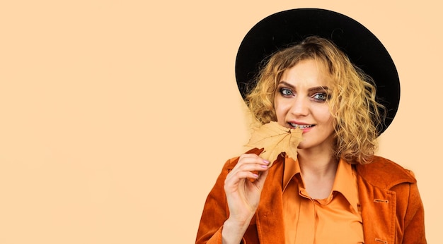 Femme sensuelle en chapeau noir et vêtements orange avec des feuilles d'automne tendance de la mode pour l'automne