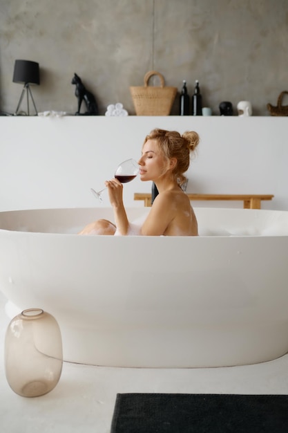 Photo femme sensuelle détendue buvant du vin rouge tout en prenant un bain avec vue arrière en mousse spa à domicile et repos le week-end ou le soir calme pour soulager le stress