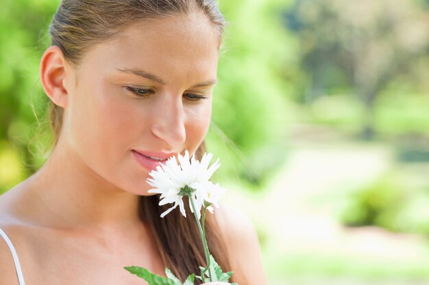 Femme sentant une fleur blanche dans le parc