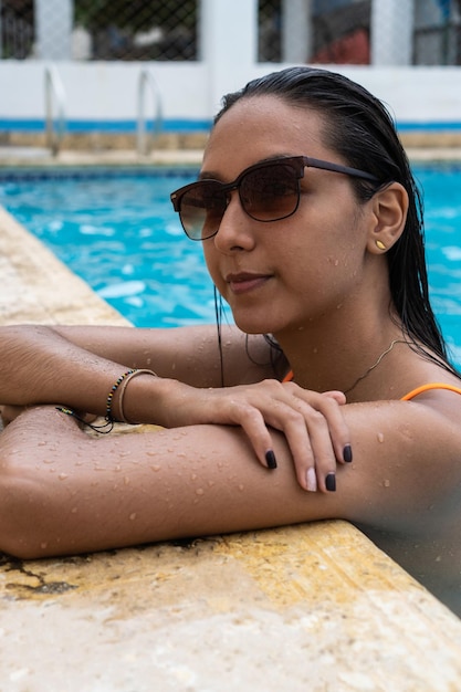 Femme sereine avec des lunettes de soleil relaxantes au bord de la piscine d'été