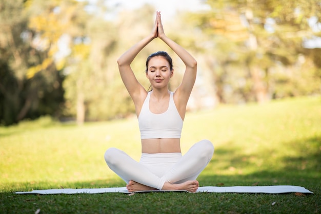 Une femme sereine en tenue de yoga blanche effectue la pose du lotus avec les yeux fermés
