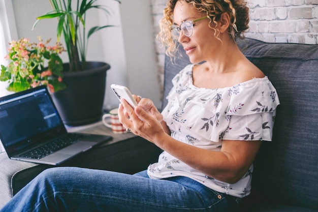 Femme sereine utilisant à la maison une connexion de téléphone portable naviguant sur Internet ou les médias sociaux avec une application moderne de gadget sur écran Ordinateur portable en arrière-plan concept de style de vie féminin moderne