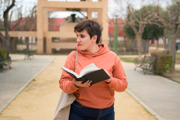 Femme sérieuse aux cheveux courts lisant un livre dans un parc