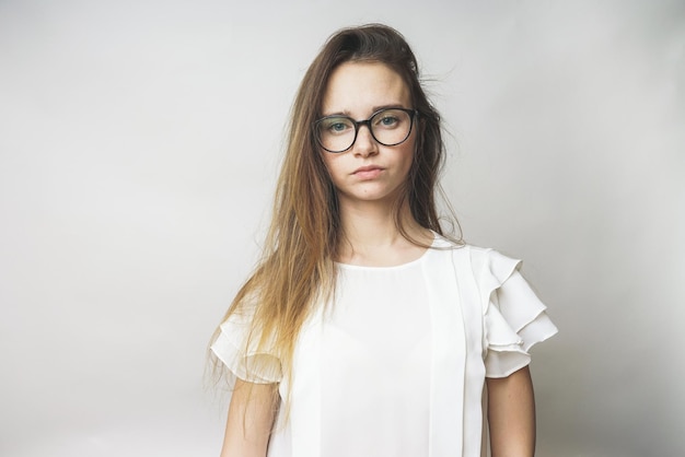 Une femme sérieuse dans un chemisier blanc regarde avec colère la caméra