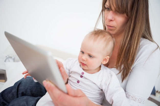 Femme sérieuse tenant son bébé tout en utilisant un tablet pc