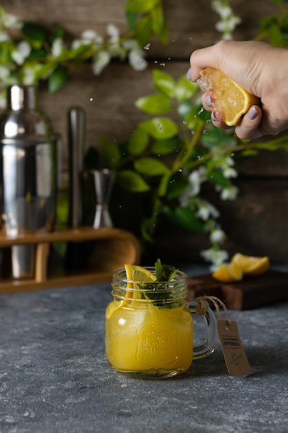 Une femme serre une orange sur un verre de jus d'orange contre un mur en bois avec des fleurs