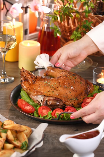 Femme servant de la dinde au pilon cuite sur un plateau de légumes sur la table à manger Happy Thanksgiving