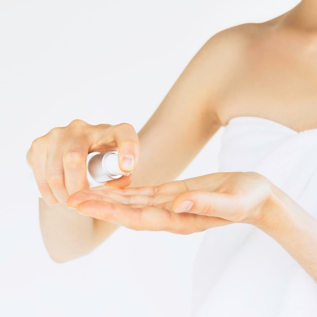 femme en serviette blanche après la douche appliquer une crème pour les mains sur sa peau sur fond blanc