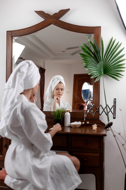 Une femme avec une serviette sur la tête et dans un manteau blanc pose alors qu'il était assis à une coiffeuse marron