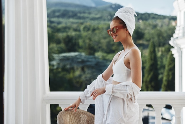 Femme avec une serviette sur la tête portant des lunettes de soleil sur le balcon avec vue sur la montagne