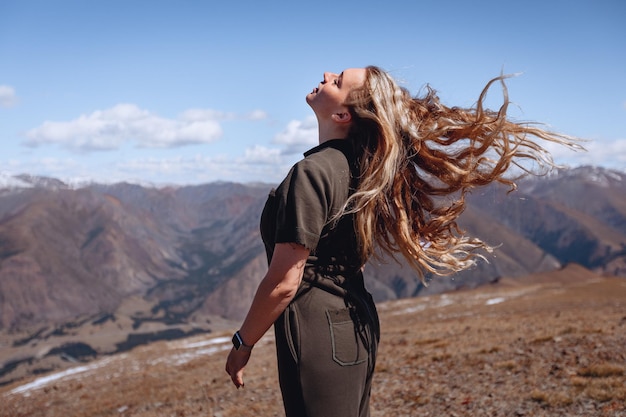 Une femme avec ses cheveux au vent se dresse sur une colline surplombant les montagnes rocheuses pittoresques