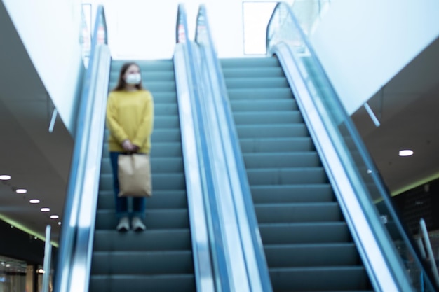 Femme seule dans un masque de protection debout sur la photo des marches de l'escalator avec un fond