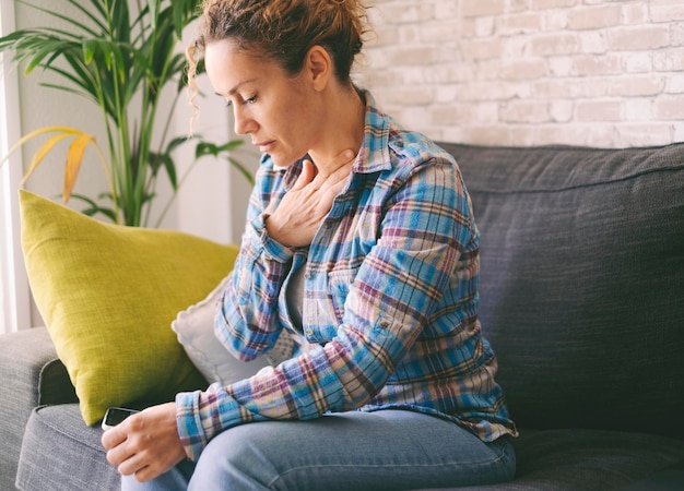 Une femme seule à la maison se touchant la poitrine pour avoir souffert de crise de panique et de problèmes d'anxiété Personnes ayant une mauvaise santé mentale et un état d'esprit dépressif Femme assise sur un canapé à la maison stressée et fatiguée