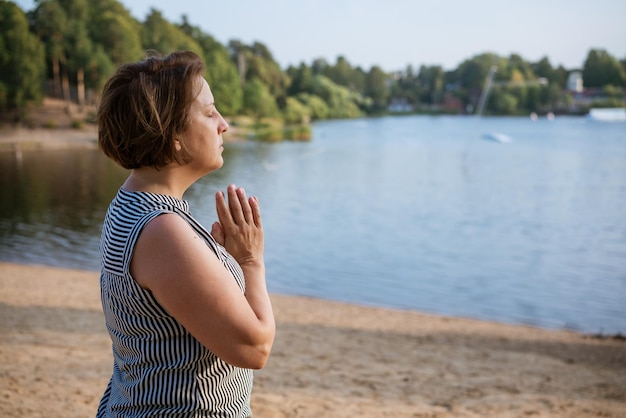 Une femme seule médite assise sur le lac de la rive avec ses paumes jointes devant