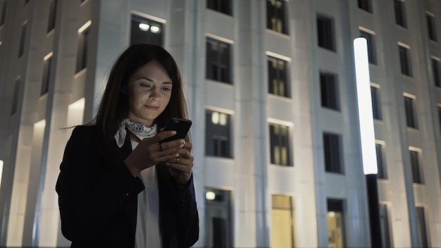 Femme seule tenant un téléphone portant une veste noire et un foulard photo de nuit