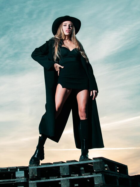 Femme sexy en chapeau de manteau de mode noir et bottes de chaussures noires belle jeune femme en robe de mode ou