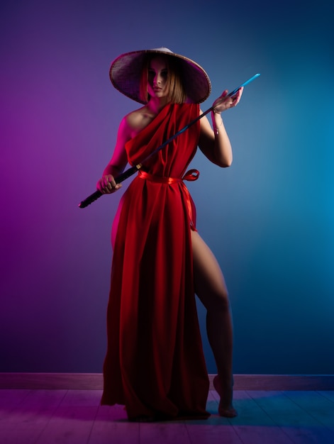 La femme sexy dans une cape rouge et un chapeau asiatique avec un katana dans sa main image d'un samouraï en couleur néon