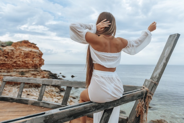 Femme sexy dans une robe blanche à un navire naufragé sur un bord de mer rocheux