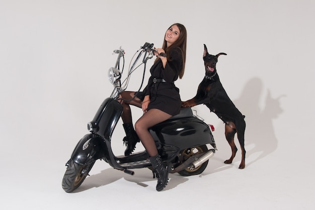 Une femme sexy est assise sur une moto. Un Doberman noir garde la maîtresse