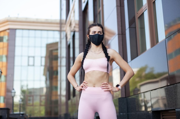 Une femme sexy et en forme avec un masque noir dans la ville faisant de l'exercice pendant la pandémie de COVID-19 ou la pollution de l'air