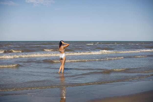 Une femme sexy en maillot de bain argenté et lunettes de soleil se tient sur la plage en été