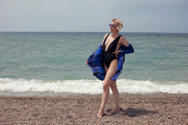 Une femme sexy en maillot de bain noir et lunettes de soleil se tient sur la plage en été