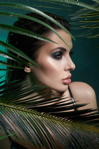 Femme sexy de portrait tropical en feuilles de palmier. Maquillage vert vif, ombre de feuilles de palmier sur le visage de la fille. Beau maquillage